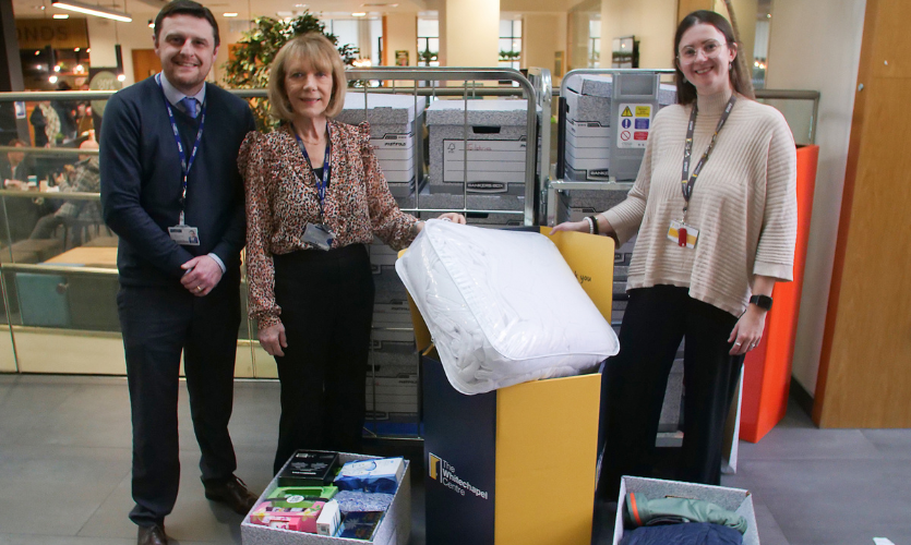 Three people stood up in front of trolleys that contain boxes full of donated items for a homeless charity 